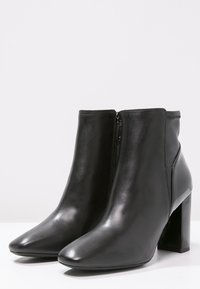 Czarne skórzane botki za kostkę z wydłużonym noskiem i masywnym, wysokim obcasem. Posiadają zamek błyskawiczny po boku oraz gładką fakturę.