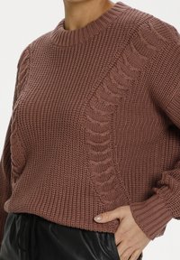 Sweter tkany w kolorze stonowanej różu z teksturowanym wzorem, z prążkowym dekoltem i mankietami oraz detalem w warkocz z boku.