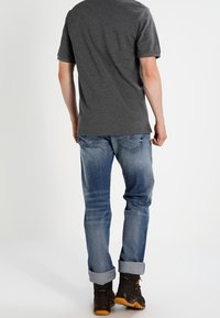 Grå t-shirt med kort ärm i kombination med uppvikta blå jeans. Bruna stövlar med svarta accenter synliga vid ankeln.