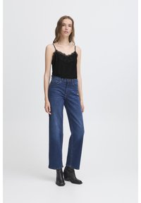 Schwarzes Trägeroberteil mit Spitzenbesatz, kombiniert mit hochgeschnittenen, blauen Jeans im weit geschnittenen Stil und schwarzen spitzen Stiefeletten. Minimalistisches Design, lässige Passform.