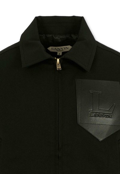 Zwarte jas met ritssluiting, puntige kraag en een leren borstzak met textuur, voorzien van een geperst "L" en "LANVIN" logo.