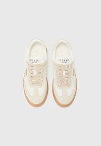 White and beige sneakers with suede accents, round toe, lace-up design, and rubber sole. "GUESS EST. 1981" label on the tongue.