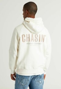 Off-white hoodie van zacht katoen met een kangoeroe-pocket. Beschikt over een opvallende grafische print op de achterkant met "CHASIN'" in lichtbruin.