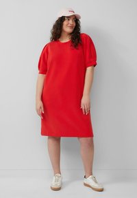 Rode oversized jurk met korte puffmouwen, gemaakt van zachte stof. Gecombineerd met een lichtroze pet en witte sneakers. Glad, eenvoudig ontwerp.