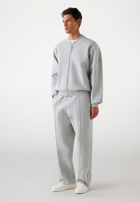 Light gray zip-up sweatshirt with elastic cuffs, paired with matching tapered pants featuring side pockets and contrasting stitch details.