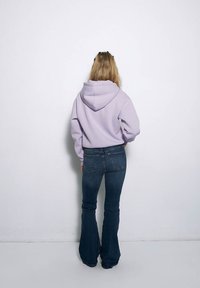 Fioletowa bluza z kapturem o dużym kapturze i szerokich rękawach, zestawiona z dopasowanymi, ciemnoniebieskimi dżinsami w stylu dzwonów. Prosty design, gładka tekstura.