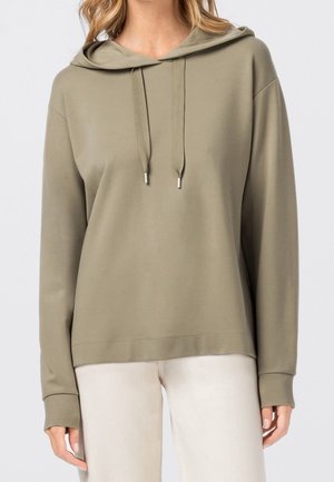 Femme portant un sweat à capuche à manches longues vert olive avec cordons, associée à un pantalon beige clair, vue des épaules jusqu'aux hanches.