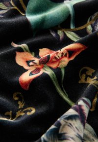 Tessuto strutturato con sfondo nero che presenta motivi floreali colorati in arancione e verde, con dettagli dorati intricati visibili.