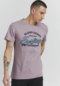 Lys lilla bomull T-skjorte med rund hals. Har et grafisk trykk som inkluderer "Blend Denim" og "Surfing" i kontrasterende farger.