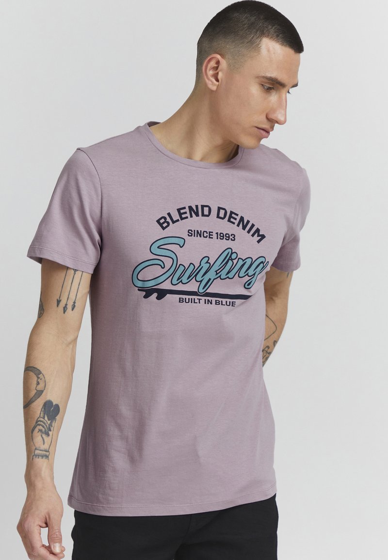 Lys lilla bomull T-skjorte med rund hals. Har et grafisk trykk som inkluderer "Blend Denim" og "Surfing" i kontrasterende farger.