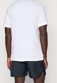 Camiseta blanca con cuello redondo y mangas cortas, combinada con pantalones cortos oscuros. El material parece suave y liso, con un diseño sencillo.