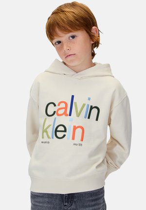 Sweat à capuche couleur crème arborant le texte multicolore « calvin klein » avec des variations de couleur et de style de police. Matière en coton, coupe décontractée.