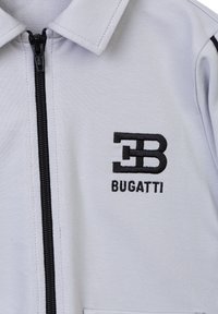 Giacca zip-up grigia chiara con logo "B" ricamato in nero accanto alla scritta "BUGATTI", con colletto strutturato e texture liscia.