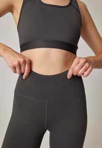 Ciemnoszare legginsy sportowe z wysokim stanem, gładką fakturą i subtelnymi przeszyciami. W zestawie z dopasowanym sportowym stanikiem.