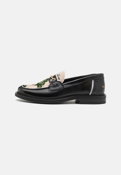 Black leather loafer featuring a textured, patterned textile upper in beige and green, with a gold-tone hardware accent and flat heel.