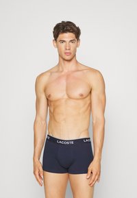 Boxers en coton bleu marine avec une ceinture élastique blanche arborant le logo Lacoste. Design ajusté avec une texture lisse.