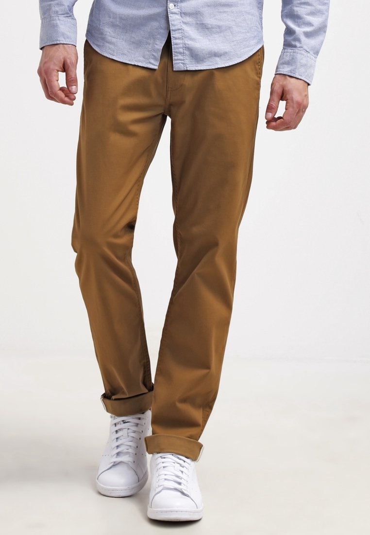 Hellbraune Chinos aus leichtem Stoff mit geradem Schnitt, umgeschlagenen Säumen und kombiniert mit weißen Turnschuhen.