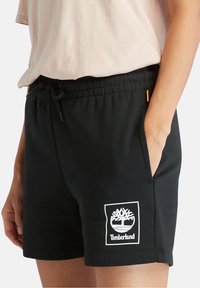 Shorts noirs en coton avec une taille élastique, des poches avant et un logo Timberland blanc. Texture douce, design décontracté.