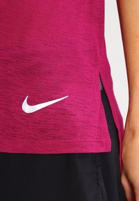 Magnetově růžové sportovní tričko s texturovaným vzorem, s bílým logem Nike na spodní levé straně a rozparky na lemu.