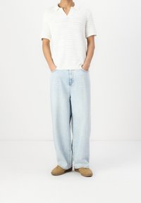 Biała krótki rękaw polo z dzianiny w serek, w połączeniu z jasnoniebieskimi luźnymi dżinsami i beżowymi trampkami. Prosty krój i faktura.