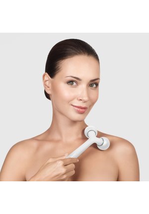 Kvinde med klar hud, der bruger hvid håndholdt ansigtsrulle på skulderen mod ensfarvet baggrund.