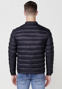 Chaqueta acolchada azul marino con diseño de acolchado horizontal, textura suave y puños abotonados, combinada con jeans de color azul claro.