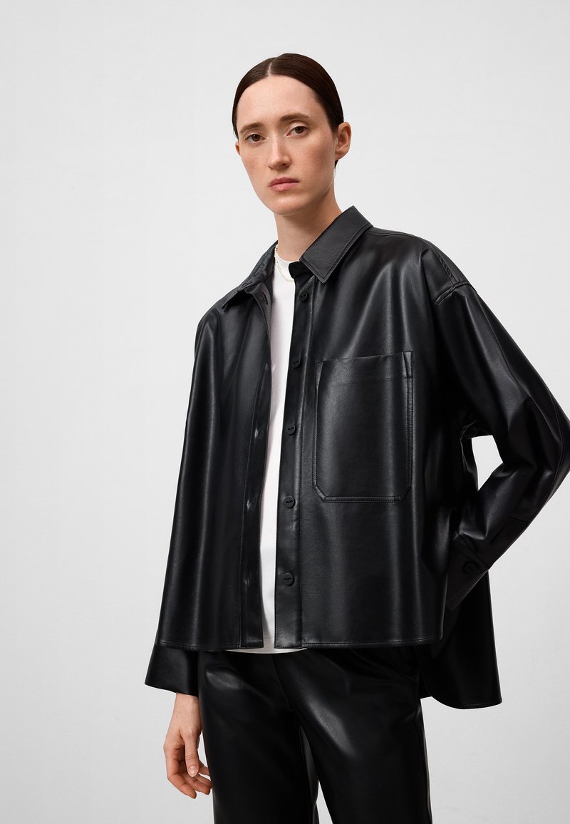 Schwarze synthetische Lederjacke mit spitzem Kragen, Fronttasche und Knopfverschluss, kombiniert mit schwarzen Hosen.