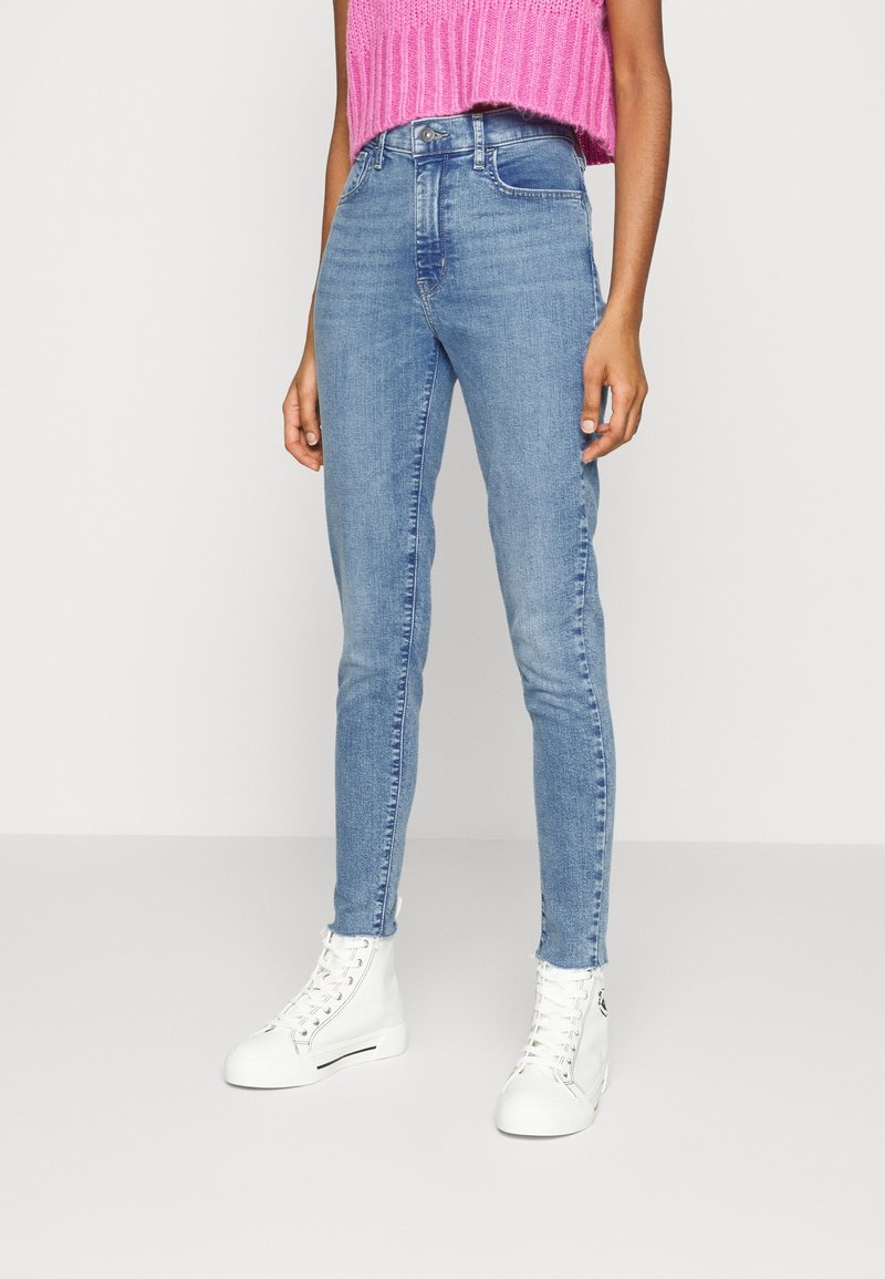 Jeans skinny blu chiaro in denim con vita alta, dotati di un design a cinque tasche e abbinati a sneaker alte bianche.