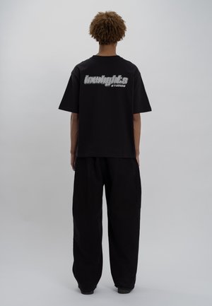 T-shirt en coton noir arborant un grand texte graphique argenté "lowlights" avec "studios" en dessous au dos. Associé à un pantalon noir ample.