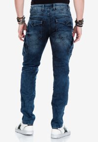 Blauwe denim cargobroek met meerdere zakken, een gestructureerde afwerking en een slim fit. Gemaakt met witte sneakers met zwarte accenten.