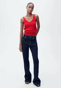 Top in maglia a coste rossa con scollo a barca abbinato a jeans a gamba larga blu scuro. Scarpe slip-on con suola piatta. Orecchini semplici ad anello.