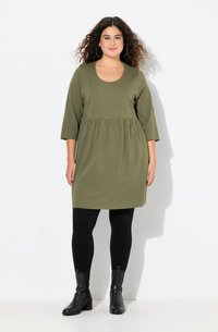 Vestido verde oliva, hasta la rodilla, con escote redondo, mangas tres cuartos y cintura fruncida. Combinado con leggings negros y botines.