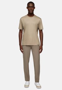 Beige crew neck t-shirt paired with beige trousers, both made from smooth fabric. White sneakers with beige accents complete the outfit.