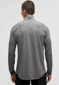 Szara, długopaśmowa koszulka sportowa z wysokim kołnierzem, teksturowanym materiałem i zaokrąglonym dołem. Charakteryzuje się eleganckim, minimalistycznym stylem bez widocznych wzorów.