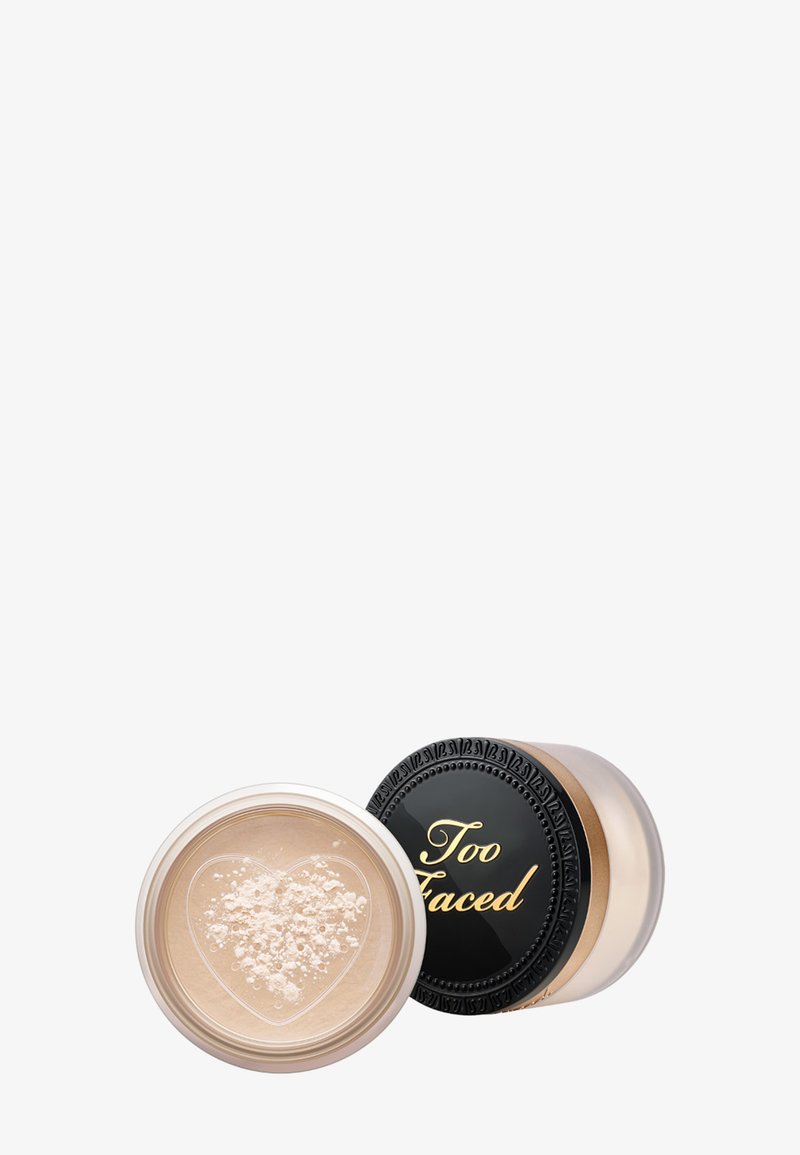 Translucente losse poeder in een doorzichtige container met een hartvormige opening; zwarte deksel met gouden tekst "Too Faced." Soepele textuur, lichte kleur.