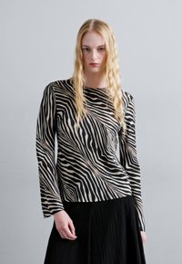 Long-sleeve top featuring a black and beige abstract zebra stripe pattern, made from a smooth fabric with a fitted cut. Pleated black skirt beneath.