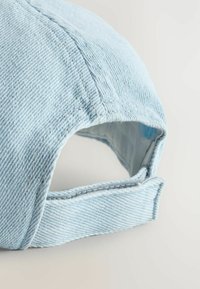 Világoskék farmer sapka varrott varrásokkal, ívelt napellenzővel és sima textúrával rendelkező állítható pánttal a hátulján.