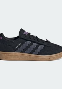 Sneaker in camoscio nero con suola in gomma color gomma, caratterizzata da strisce grigie pixelate e accenti viola sulla linguetta e sul tallone.