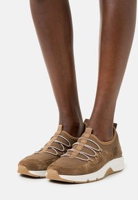 Braune Suede- und Mesh-Sportschuhe mit elastischen Schnürsenkeln, einer gepolsterten weißen Zwischensohle und einer strukturierten Sohle für besseren Halt.