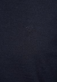 Marineblauer Strickpullover mit subtiler geprägter Logodetails, weichem Material und figurbetonter Passform.