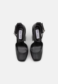 Czarne skórzane buty na wysokim obcasie z zamkniętym palcem i paskiem w kostce. Charakteryzują się grubym obcasem i gładką fakturą. Logo umieszczone na wkładce.