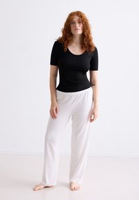 Zwart T-shirt met korte mouwen gecombineerd met losse witte pyjamabroeken. De stof is soepel en de broeken hebben een elastische tailleband.