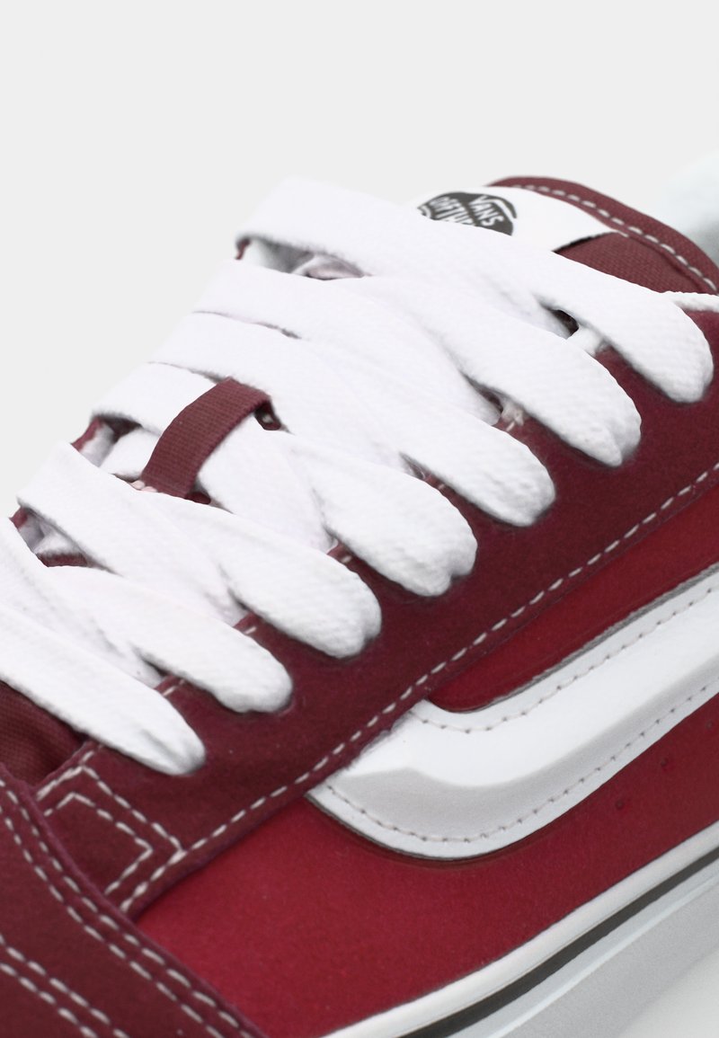 Rode canvas sneaker met witte veters, voorzien van een kenmerkend wit streeppatroon aan de zijkant en contrasterende stiksels.