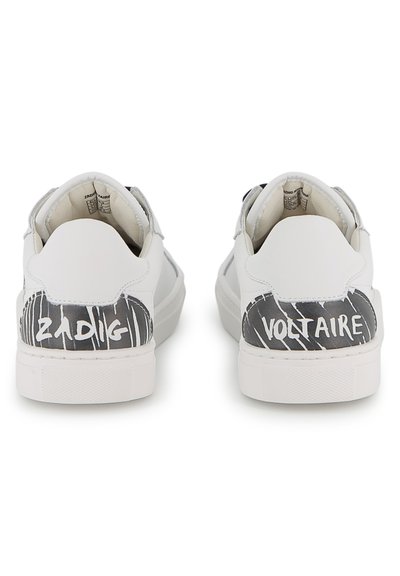 Λευκά αθλητικά παπούτσια με λείο δέρμα. Στο πίσω μέρος διαθέτουν μαύρα και λευκά γραφικά μοτίβα με τις λέξεις «ZADIG» και «VOLTAIRE» τυπωμένες. Στρογγυλεμένο σχήμα.