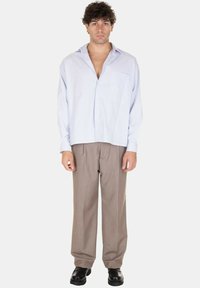 Camicia azzurra chiara, comoda e con bottoni, dotata di taschino sul petto, abbinata a pantaloni larghi marroni e scarpe nere. Tessuto semplice e testurizzato.