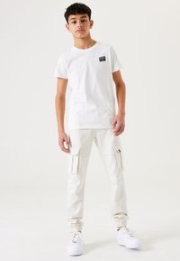 Witte t-shirt met korte mouwen en een logo patch, gecombineerd met witte cargo pants met twee zijzakken en elastische boorden. Witte sneakers.
