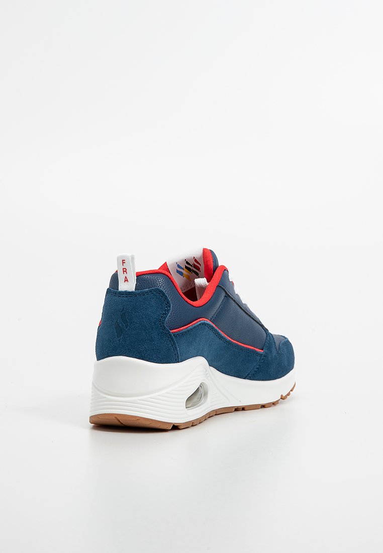Basket de sport bleu marine avec tige en suède et en maille, accents rouges et semelle intermédiaire blanche. Caractéristiques d'un talon semi-transparent et d'une semelle texturée.