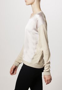 Long-sleeved sweater featuring a silky white front and beige knit sleeves, with ribbed cuffs and hem. Smooth texture and contrasting materials.