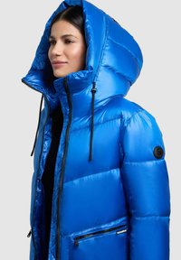 Blaues Puffy-Jacke mit glanzvollem Finish, einer großen Kapuze, schwarzem Reißverschluss und einer Reißverschlusstasche. Gesteppte Textur und elegantes Design.