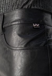 Pantalons en simili cuir noir avec une texture lisse, présentant une poche arrière et un petit accent en métal décoratif avec un motif léopard.